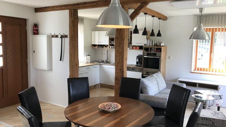 Moderner Wohnbereich mit Esstisch, St&uuml;hlen, K&uuml;che und Sofa.