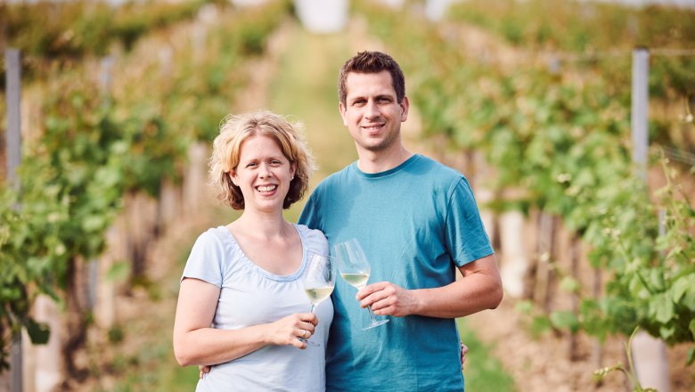Ein Paar steht in einem Weinberg und h&auml;lt Weingl&auml;ser in der Hand.