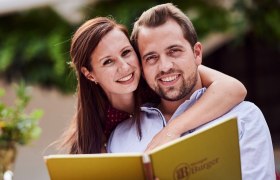 Ein l&auml;chelndes Paar h&auml;lt eine Men&uuml;karte beim Heurigen Burger.