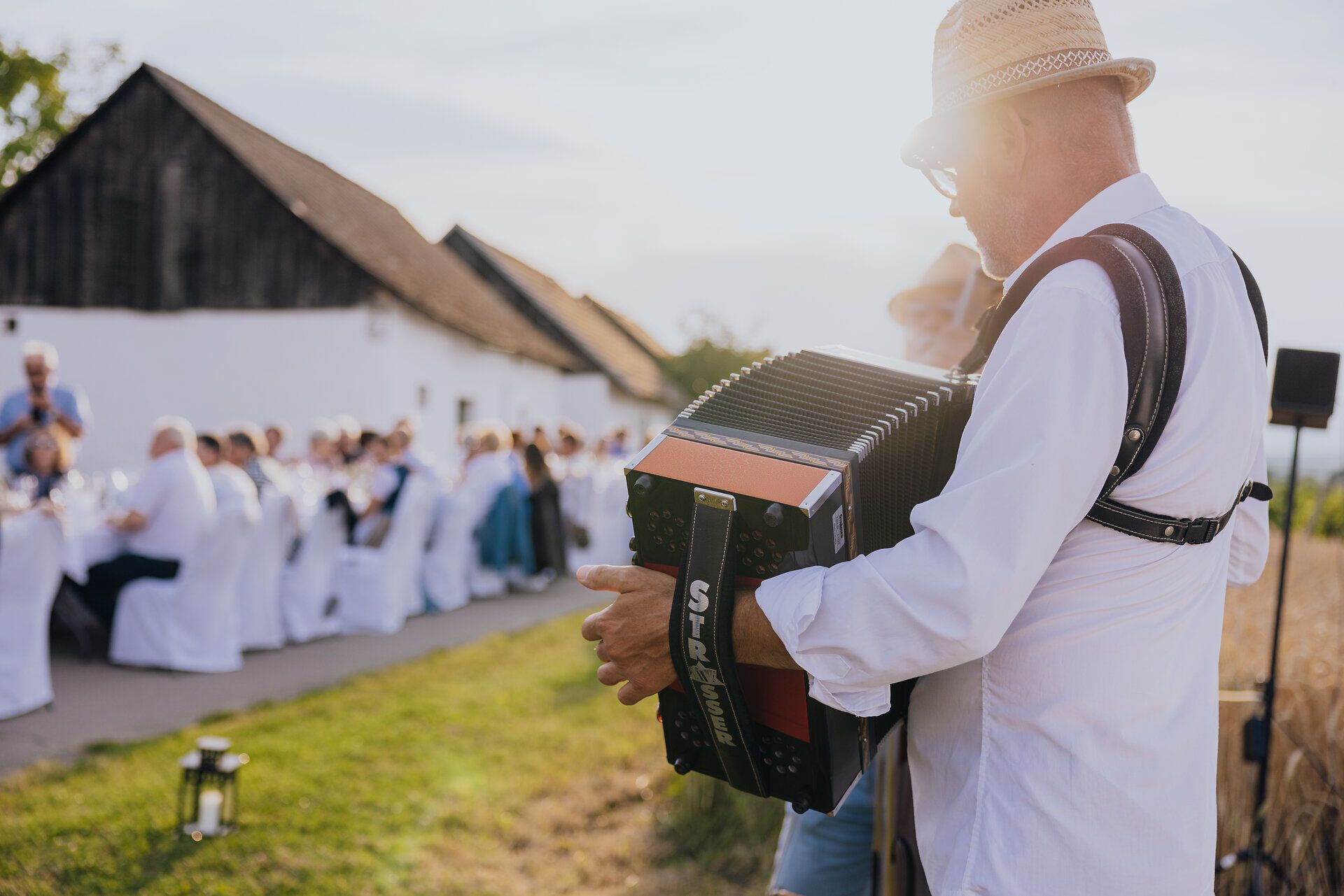 In der malerischen Kellergasse „Alte Geringen“ umgeben von sanften Weinbergen, erklingt die fröhliche Melodie eines Akkordeons. Die Gäste genießen die kulinarischen Köstlichkeiten und die entspannte Atmosphäre, während die Sonne sanft über die Landschaft strahlt.