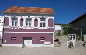 Außenansicht eines lila Hauses mit weißen Fensterrahmen und einem Schild für ein Gästehaus.