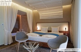 Modernes Doppelzimmer mit großem Bett, zwei grauen Stühlen und einem Glastisch.