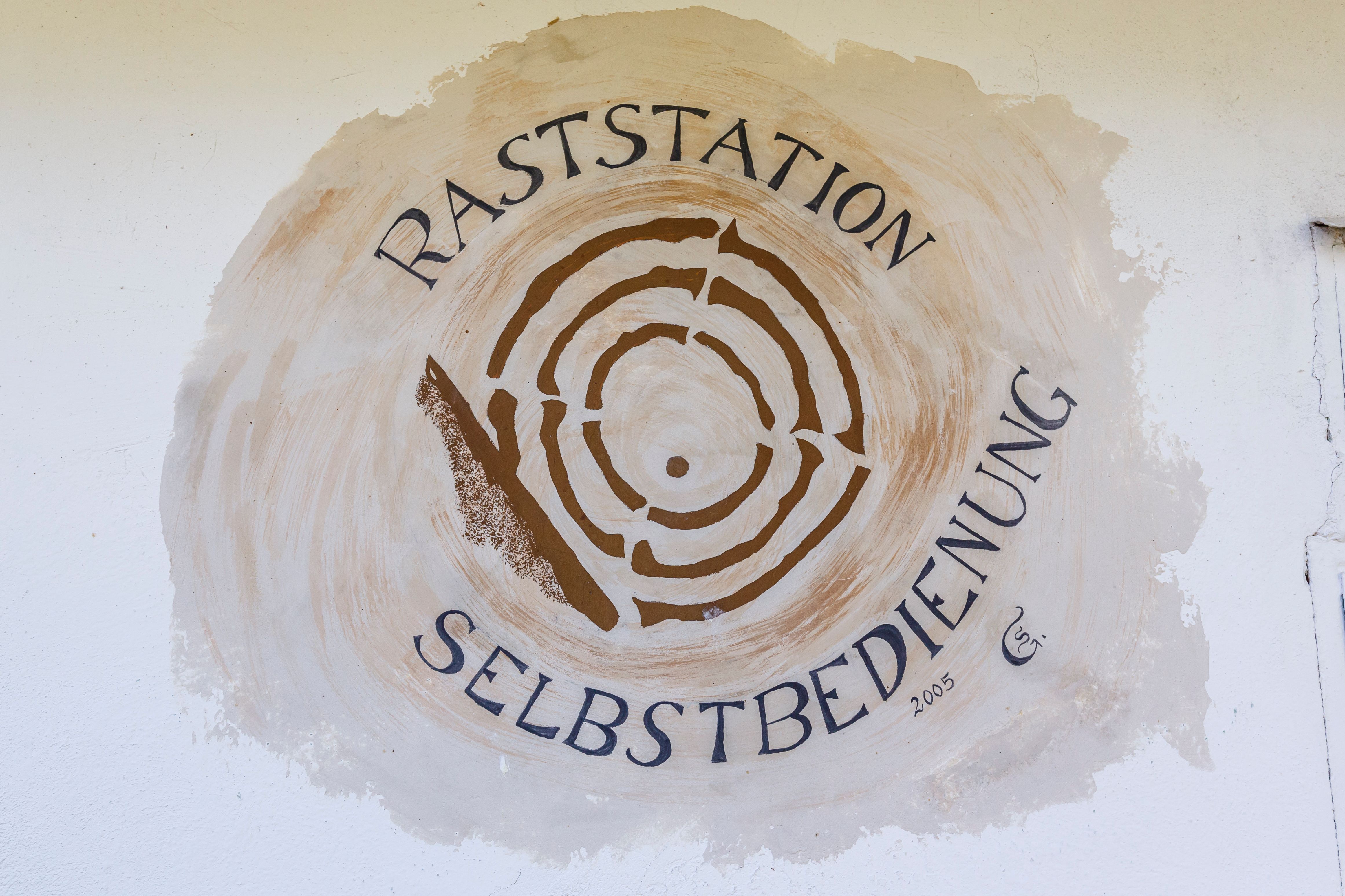 Nástěnná malba s nápisem "Raststation Selbstbedienung" a stylizovaným kmenem stromu.