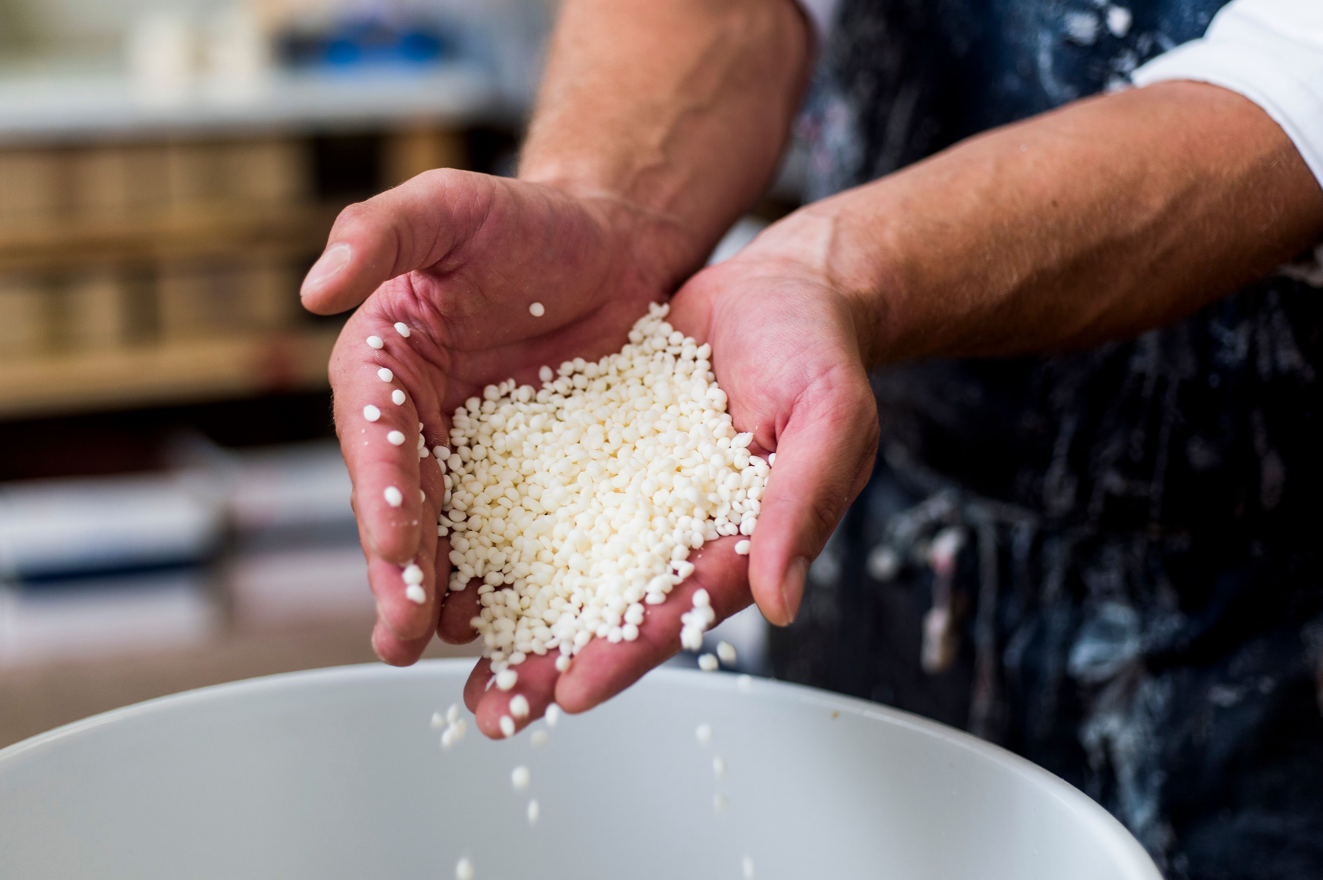 Nahaufnahme von Händen, die weiße Wachskügelchen über einem Behälter halten.