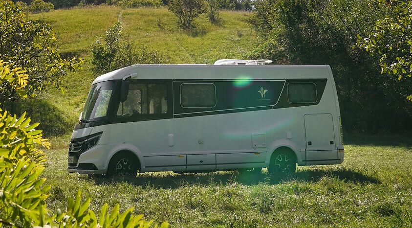 Umgeben von üppigem Grün und unter einem strahlend blauen Himmel, bietet der Campingwagen einen perfekten Rückzugsort für Naturliebhaber. Die sanften Hügel im Hintergrund und die historische Burgruine schaffen eine malerische Kulisse, die zum Entspannen und Erkunden einlädt.