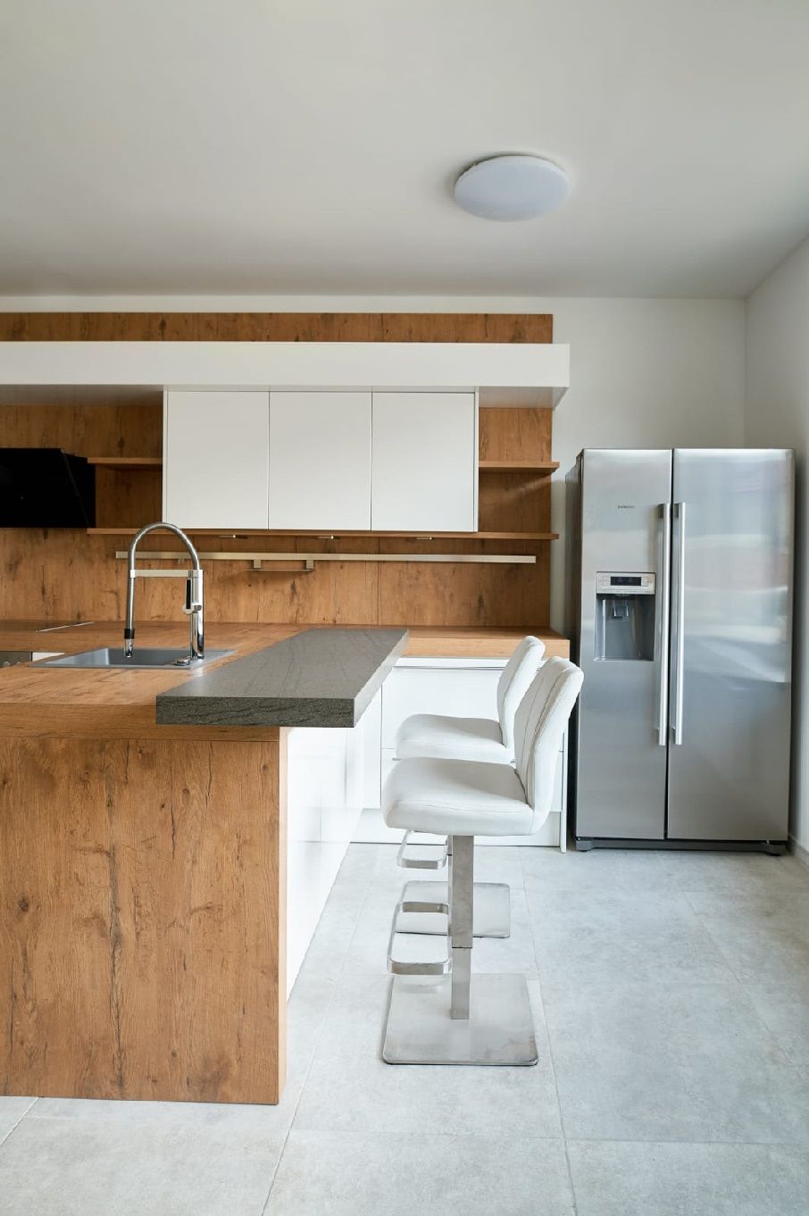 Moderne Küche mit Holz- und Weißtönen, Barhockern und Edelstahlkühlschrank.