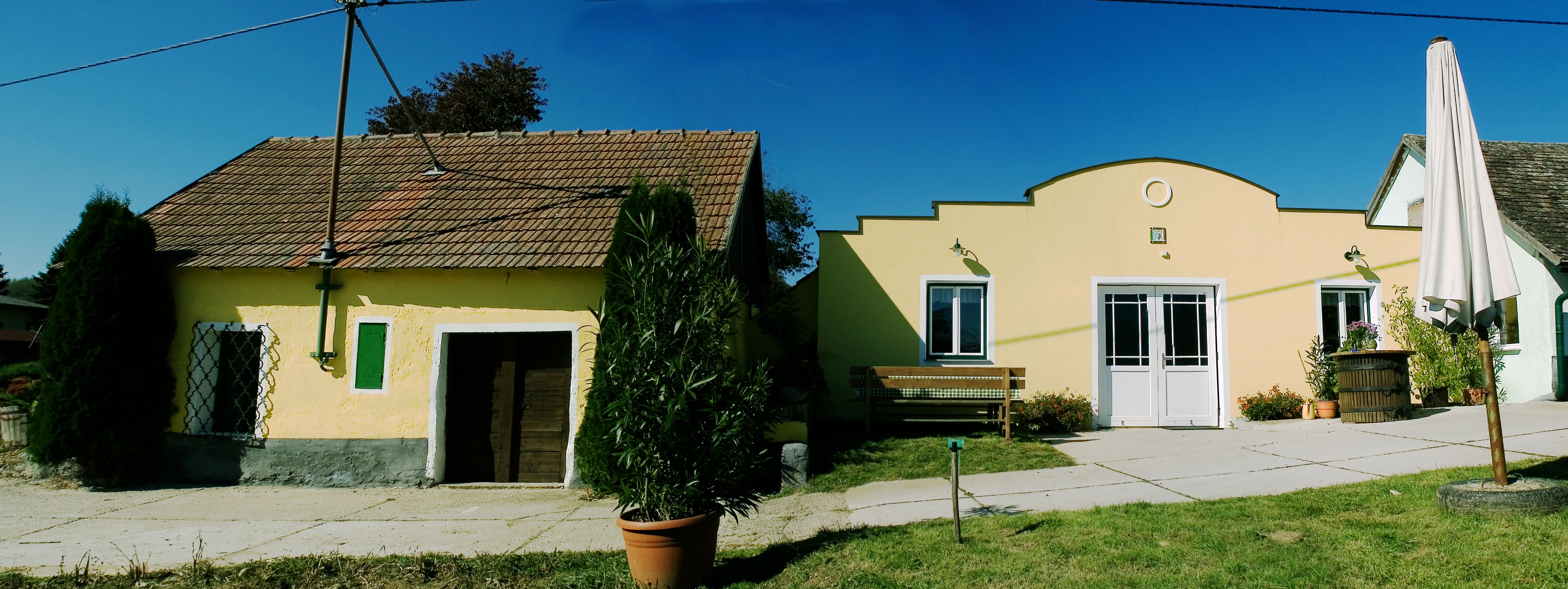 Dvě žluté budovy vinařství s taškovými střechami a rostlinami v popředí.