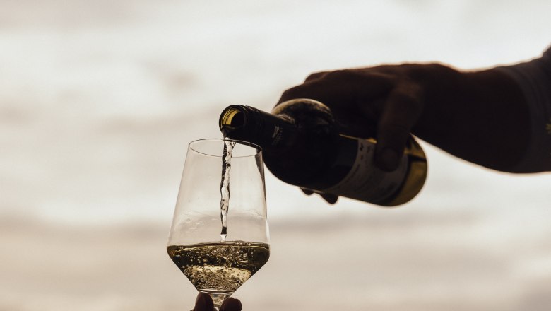 Wein wird in ein Glas im Freien eingeschenkt, im Hintergrund eine Landschaft.