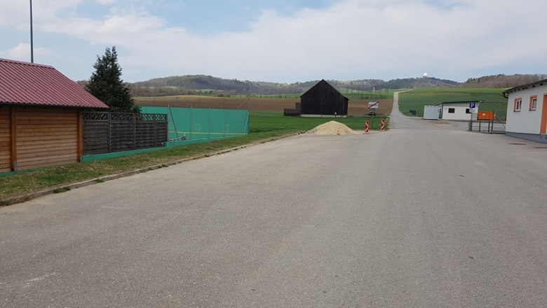 Ein leerer Parkplatz mit umliegenden Gebäuden und Feldern im Hintergrund.