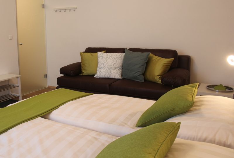 Ein gemütliches Zimmer mit einem Doppelbett und einer braunen Couch, dekoriert mit grünen und weißen Kissen.