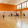 Personen spielen in einer Turnhalle Fu&szlig;ball und Basketball.