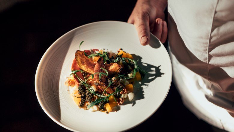 Ein Teller mit einem kunstvoll angerichteten Gericht wird von einer Person in weißer Kleidung gehalten.