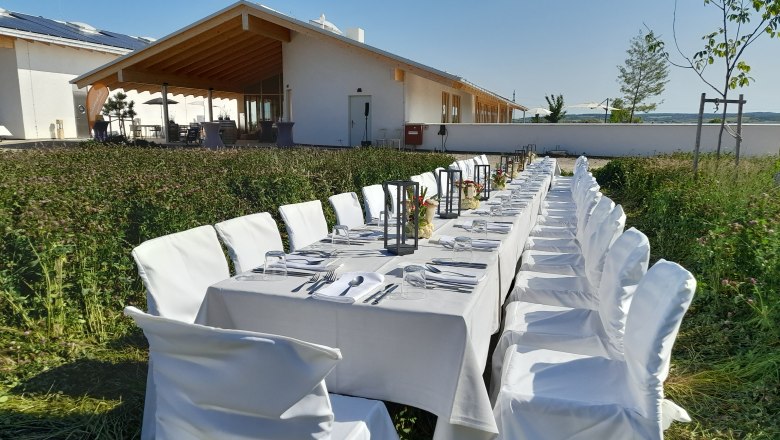 Langer, gedeckter Tisch im Freien vor einem modernen Gebäude mit Holzveranda.