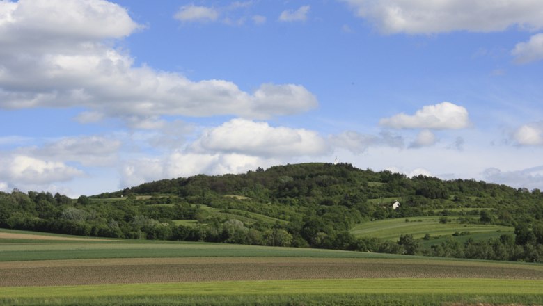 Landschaft mit Hügeln und Feldern unter blauem Himmel mit Wolken.