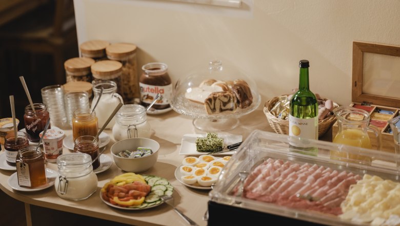 Fr&uuml;hst&uuml;cksbuffet mit Brot, Aufschnitt, Obst und Getr&auml;nken.