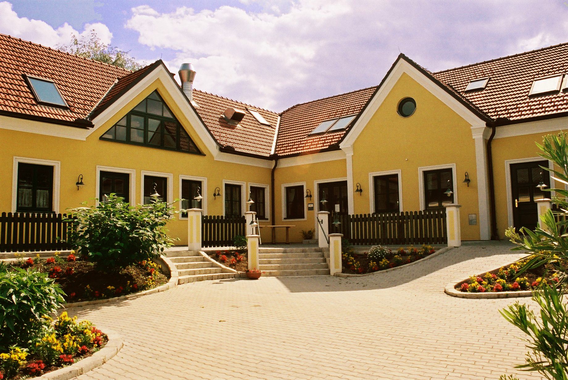 Gelbes Gebäude mit roten Ziegeldächern und Garten.