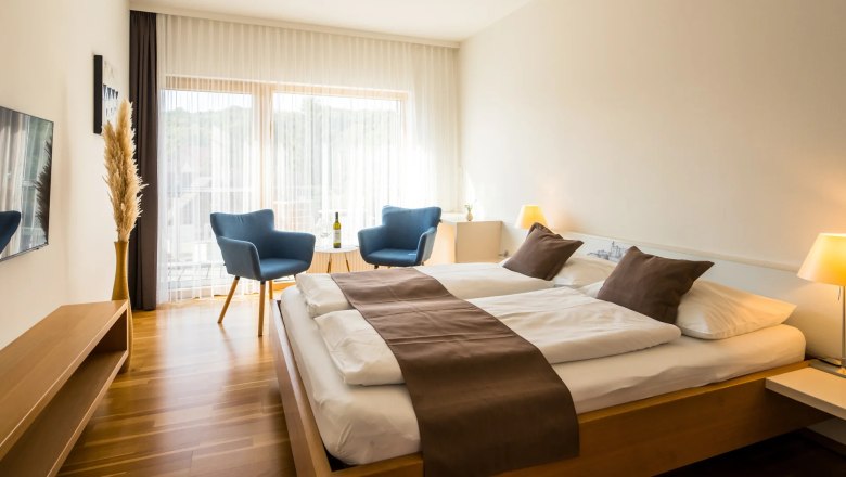 Modernes Gästezimmer mit Doppelbett, blauen Sesseln und Holzboden.