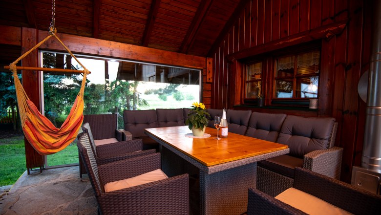 Überdachte Terrasse mit Holztisch, Rattanmöbeln und Hängesessel.