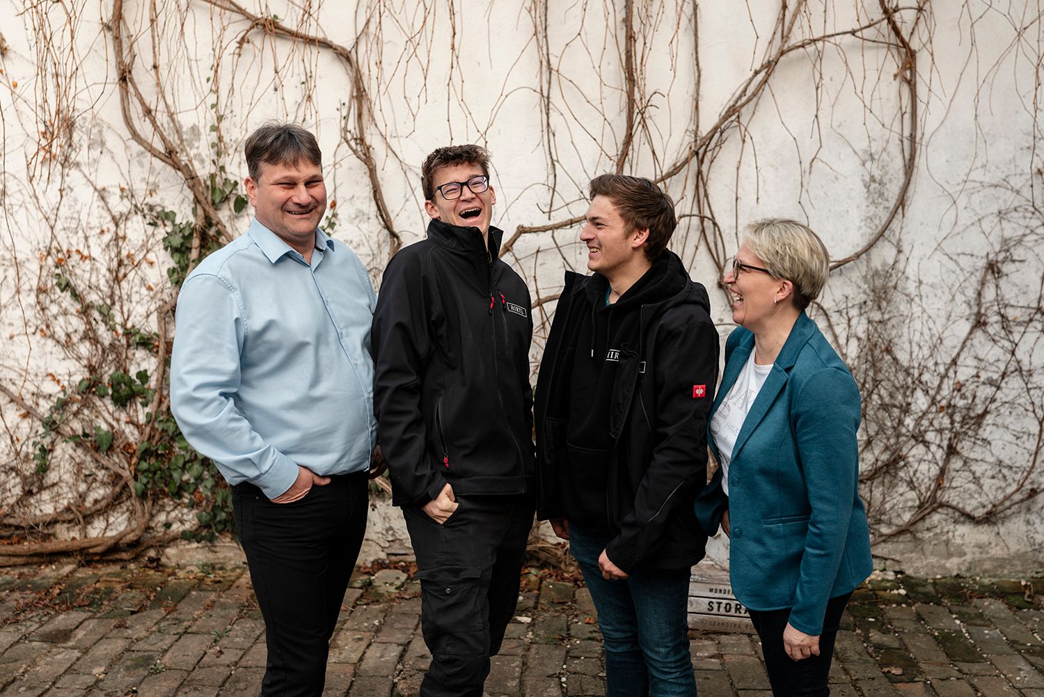 Eine Familie - bestehend aus 4 Personen - steht vor einer Mauer und unterhält sich fröhlich.