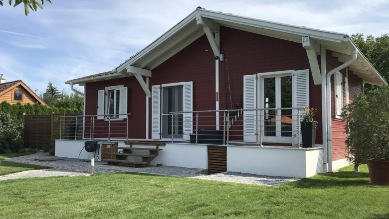 Ein rotes Holzhaus mit wei&szlig;em Dach und Fensterl&auml;den, umgeben von einem gepflegten Garten.