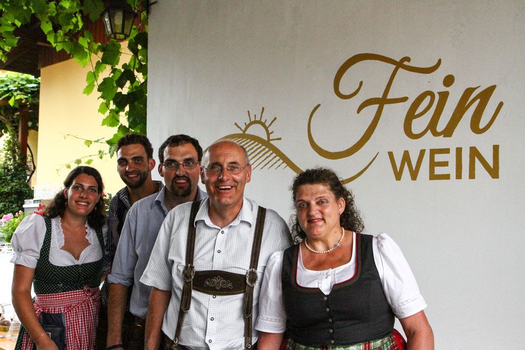 A group of five people in traditional dress in front of a sign saying 'Fein Wein'.