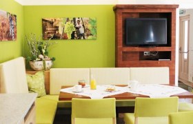 Gemütlicher Essbereich mit grünen Wänden, Holzmöbeln und einem Fernseher.