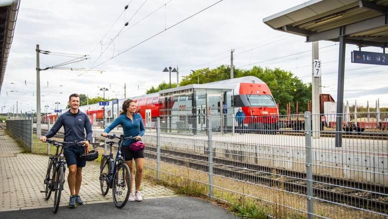 Two people with bicycles at the station, an &Ouml;BB train in the background.