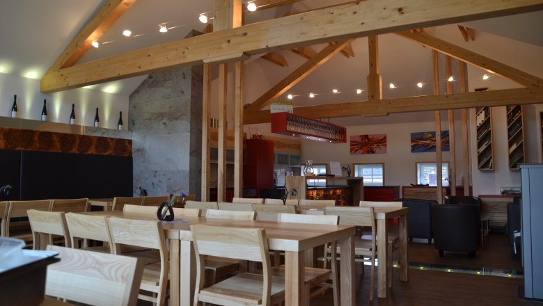 Innenansicht eines modernen Weinguts mit Holzbalken, Tischen und Stühlen.