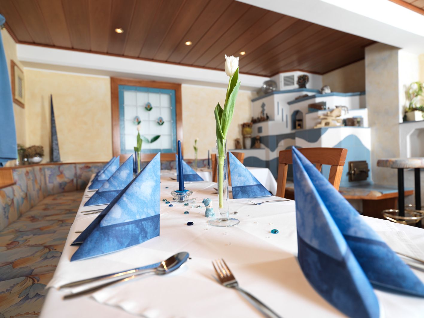 Ein elegant gedeckter Tisch in einem Restaurant mit blauen Servietten und einer weißen Tulpe in der Mitte.