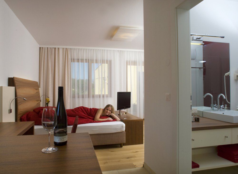 Ein modernes Hotelzimmer mit einem Bett, auf dem eine Person liegt, und einem Tisch mit einer Weinflasche und einem Glas.