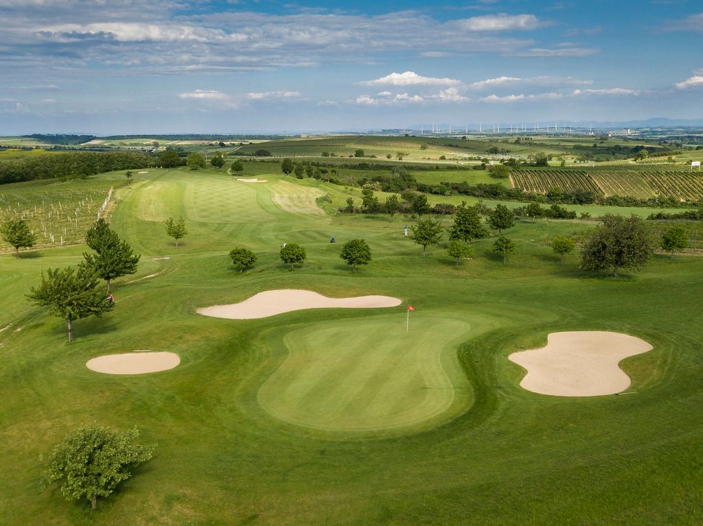 Luftaufnahme eines Golfplatzes mit Grünflächen, Sandbunkern und umliegenden Feldern.