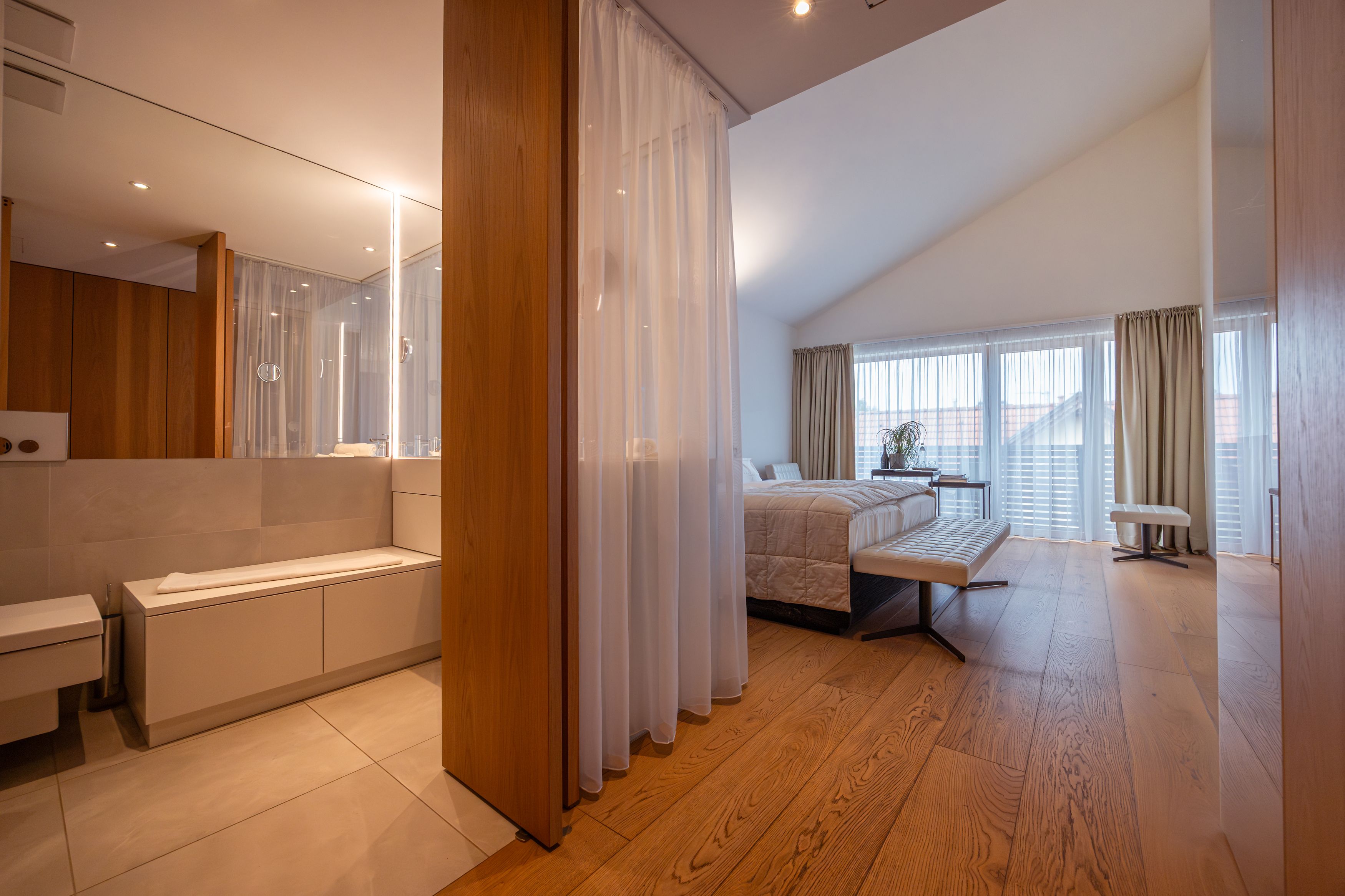 Modernes Hotelzimmer mit Holzfußboden, großem Bett und Badezimmer mit Spiegel.