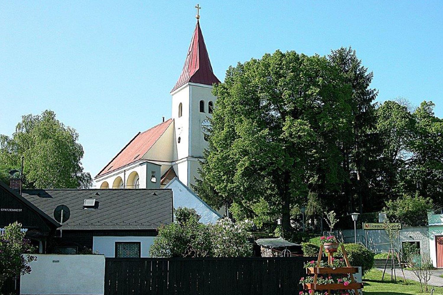 Eine Kirche mit rotem Dach und Turm, umgeben von Bäumen und Häusern.