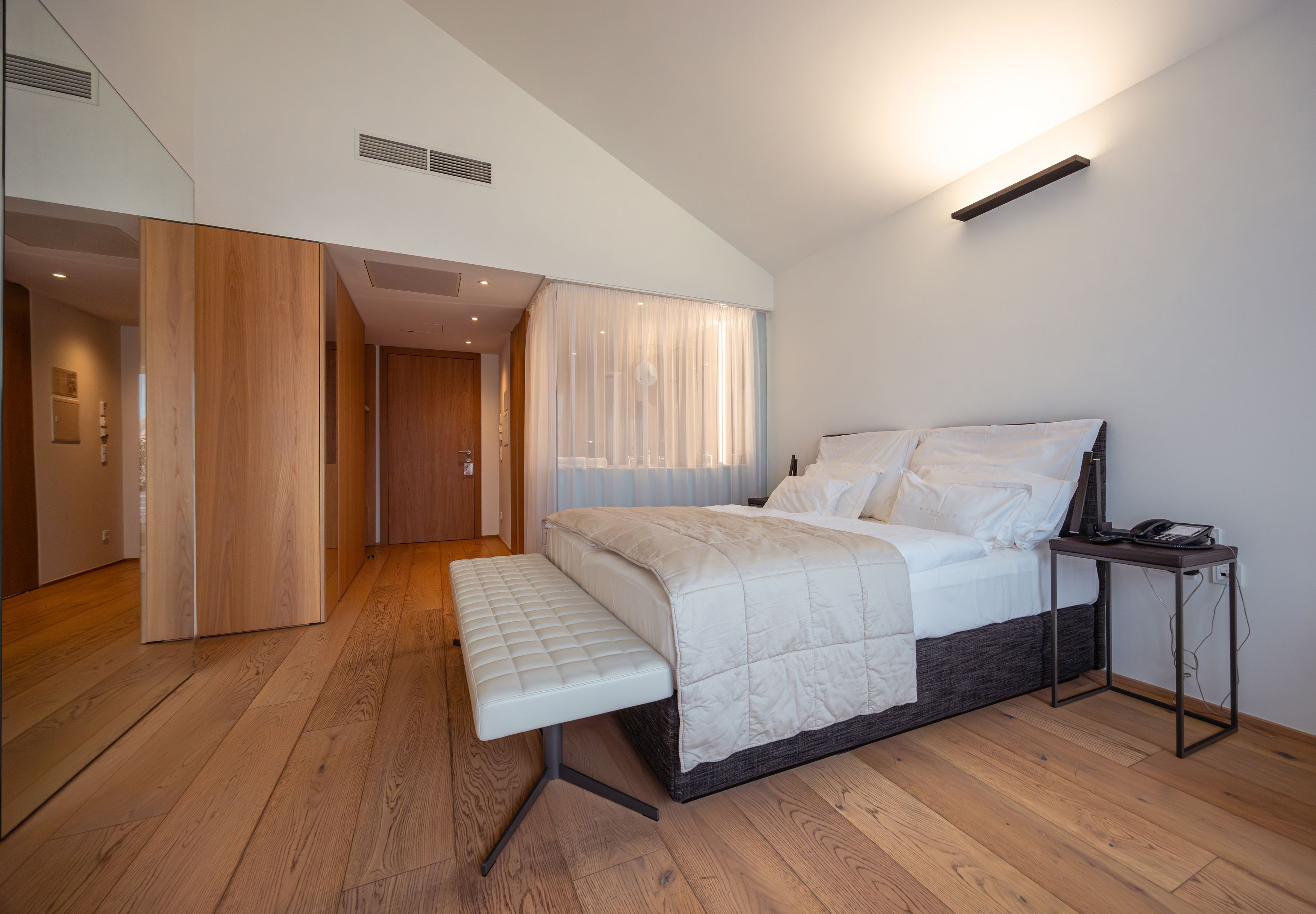 Modernes Hotelzimmer mit großem Bett, Holzboden und minimalistischer Einrichtung.