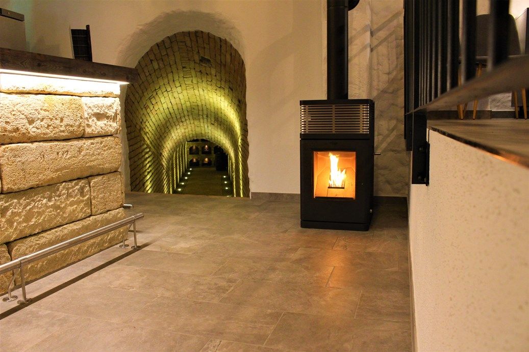 Ein Weinkeller mit beleuchtetem Gewölbegang und einem brennenden Kaminofen.