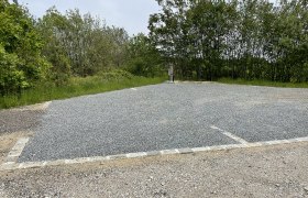 Ein leerer Wohnmobilstellplatz mit Kiesboden, umgeben von Bäumen und einer Laterne.