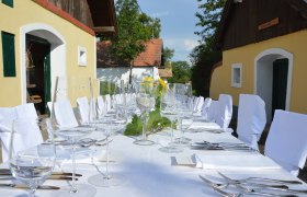 Ein festlich gedeckter Tisch im Freien mit weißen Tischdecken und Stühlen, umgeben von traditionellen Gebäuden.