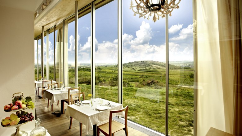 Innenansicht eines Restaurants mit großen Fenstern und Blick auf eine grüne Landschaft.