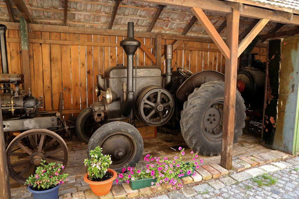 Alte Dampfmaschinen in einem Holzschuppen mit Blumen im Vordergrund.