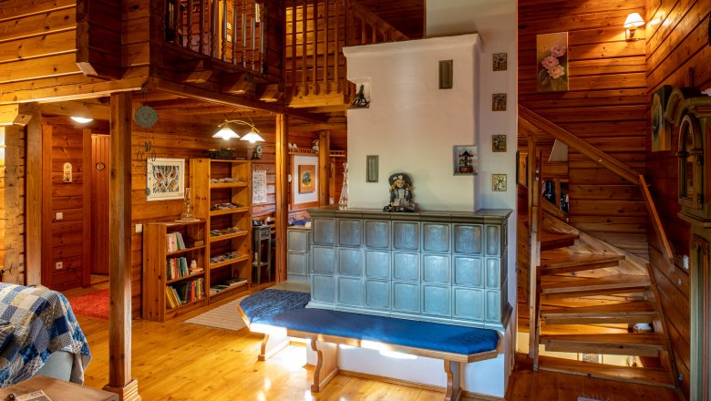 Gemütlichkeit rund um den Kachelofen, © Imre Antal Gemütliches Wohnzimmer mit Kachelofen, Holzwänden und Treppe.