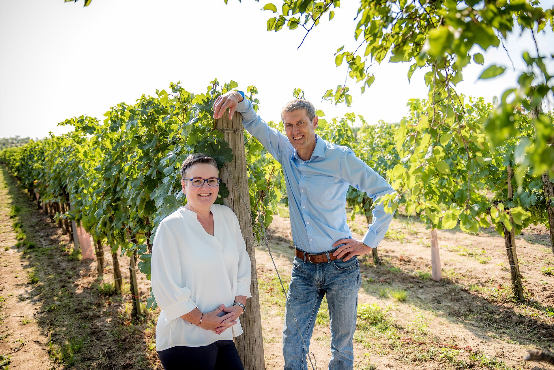 A man and a woman stand smiling in a vineyard.