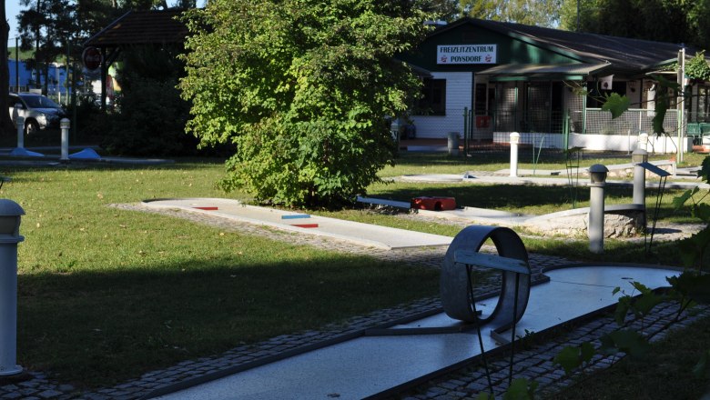 Minigolfplatz mit Hindernissen und einem Gebäude im Hintergrund.