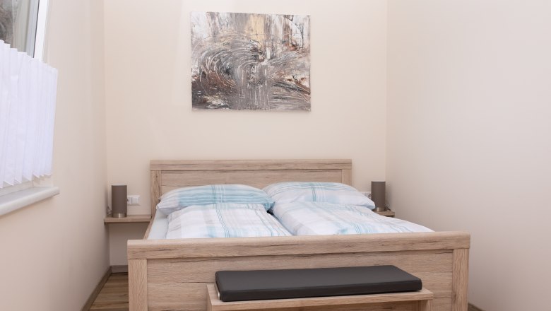Schlafzimmer mit Doppelbett, Holzm&ouml;beln und abstraktem Kunstwerk an der Wand.