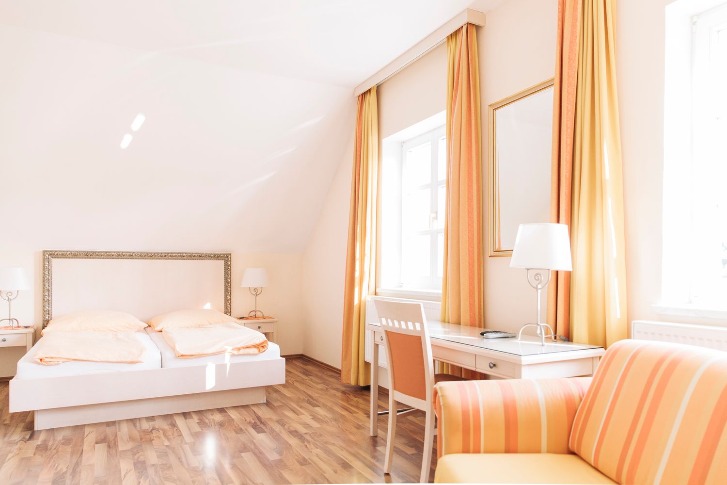 Helles Gästezimmer mit Doppelbett, Schreibtisch und Sofa in warmen Gelbtönen.