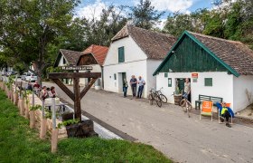 Weinkellerstraße in Mailberg mit Menschen, Fahrrädern und einem Schild 'Radlerrast'.
