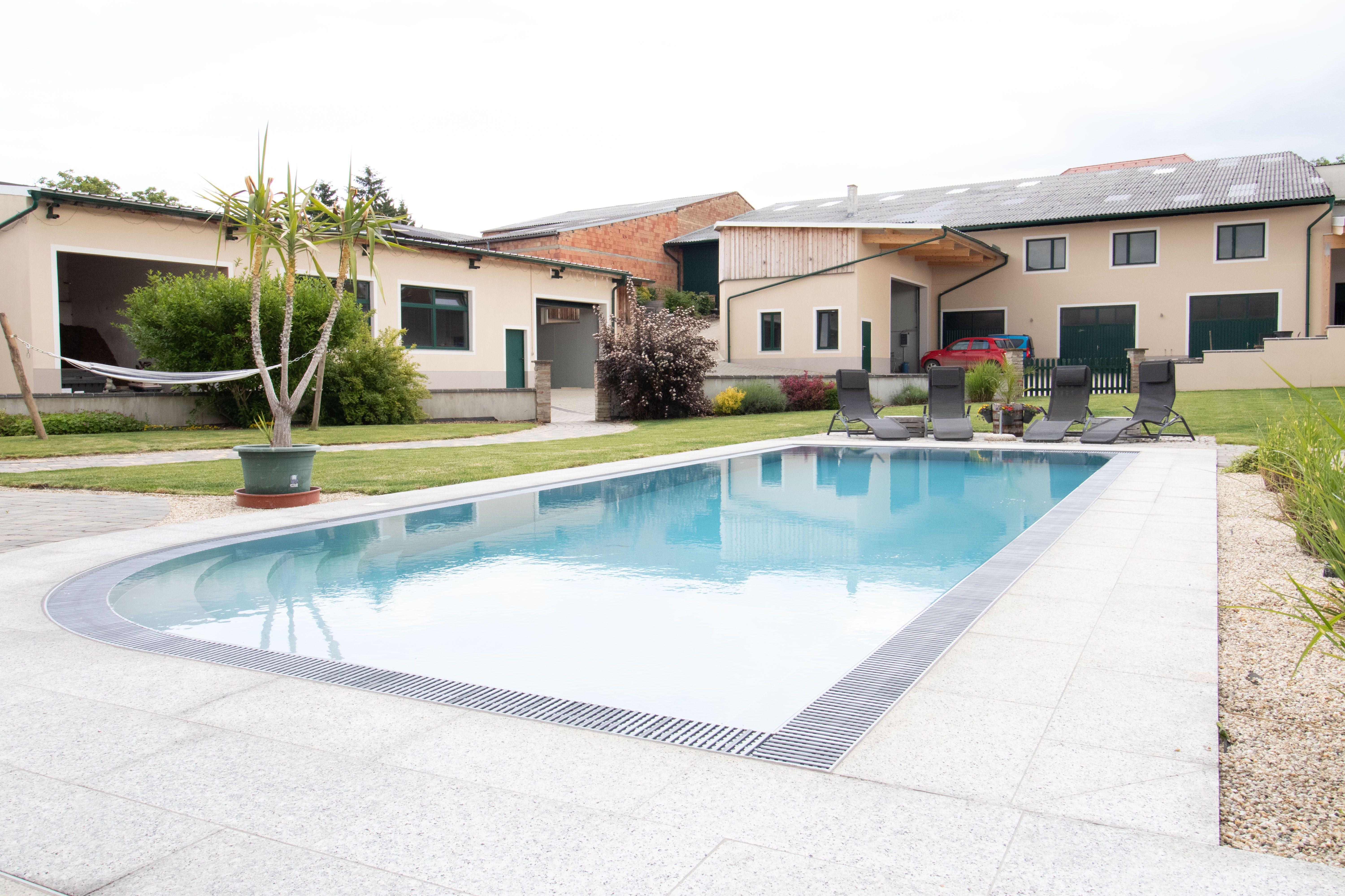 Ein moderner Hof mit einem großen Swimmingpool und Liegestühlen im Vordergrund.