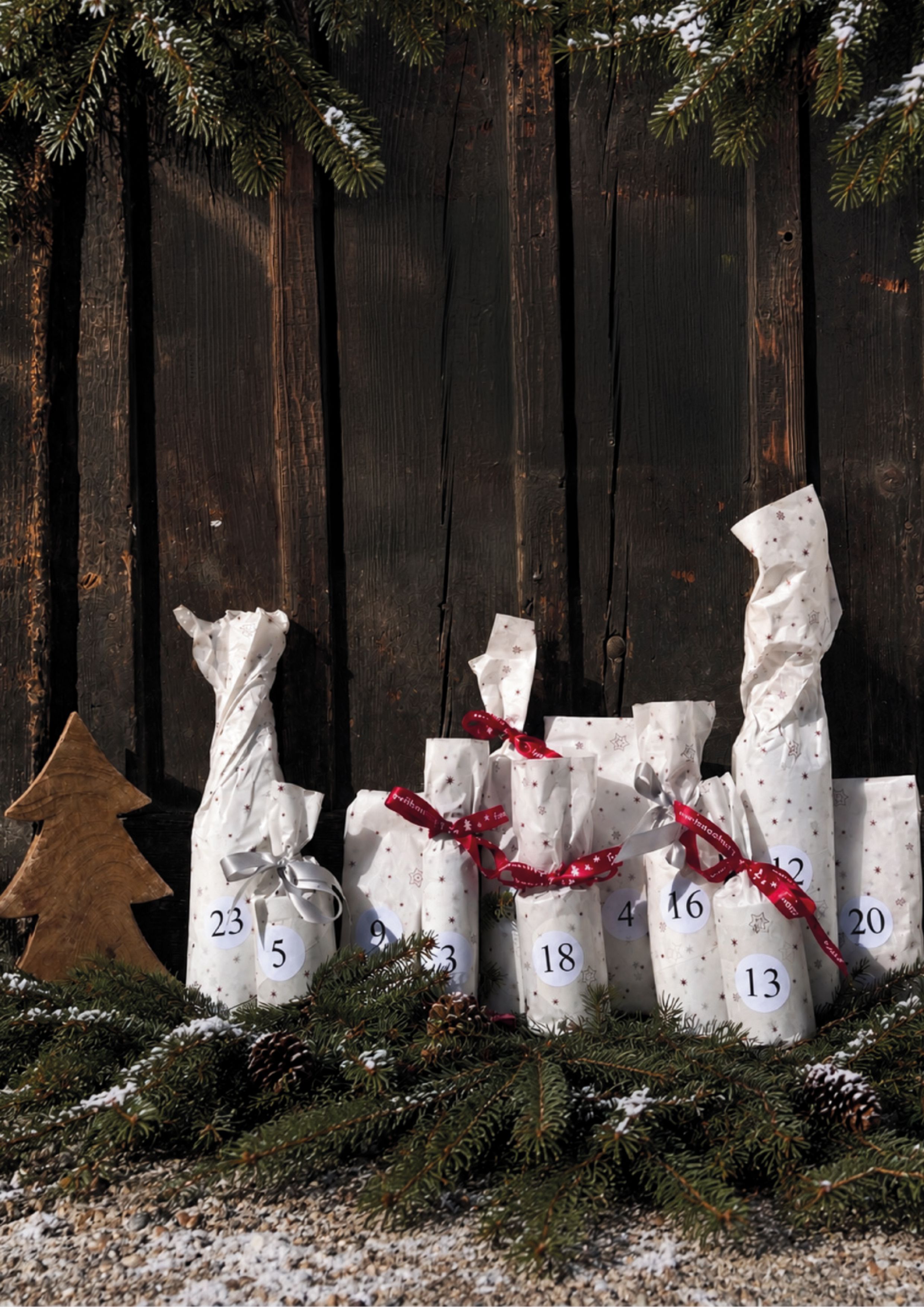 Adventkalender mit kleinen Geschenk-Päckchen aufgestellt vor einer Holzwand