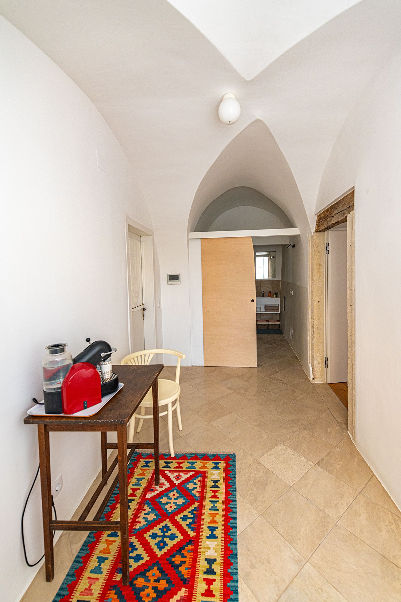 Eingangsbereich mit Tisch, Stuhl und buntem Teppich.