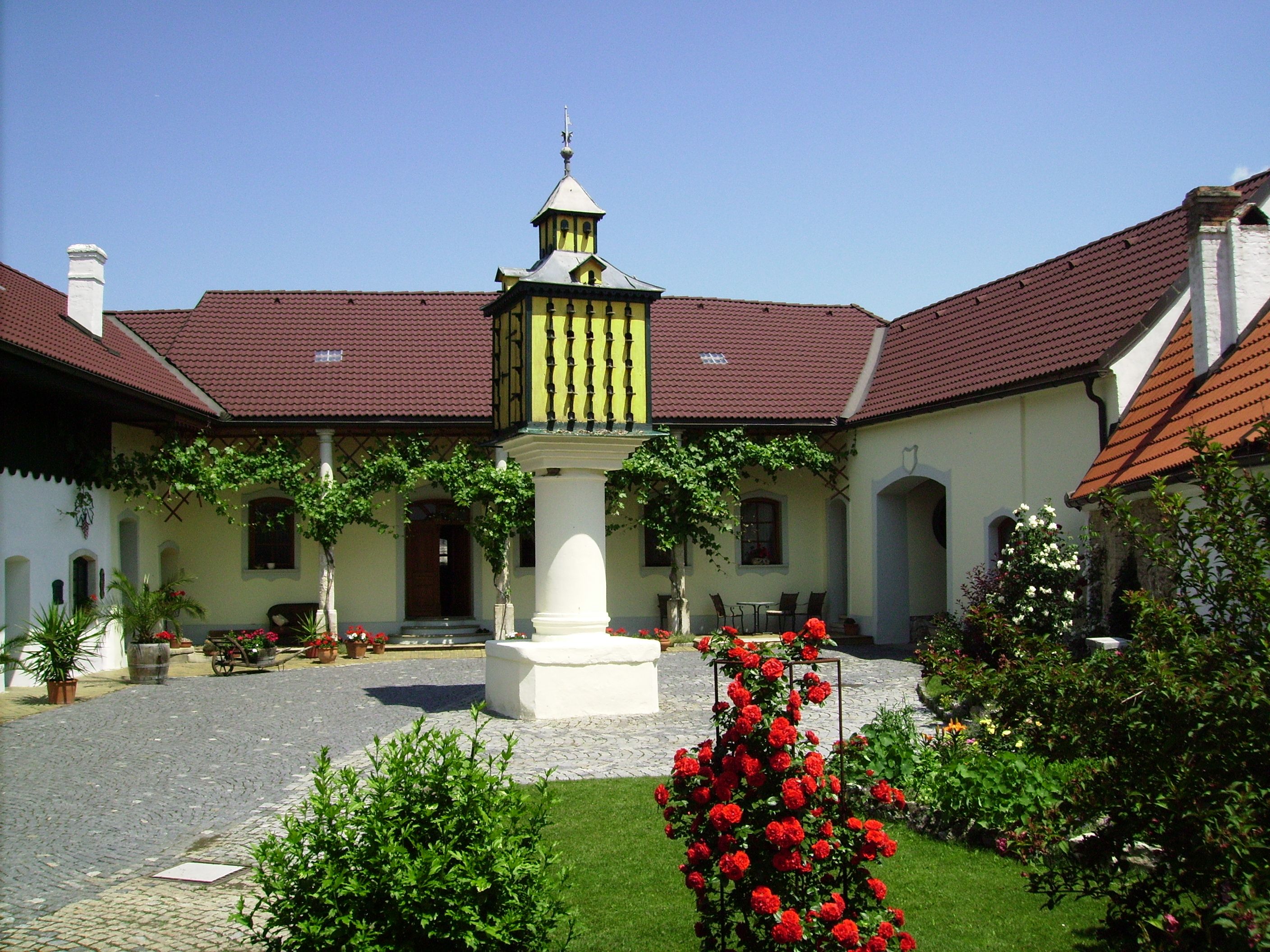 Upravené nádvorie s kvetmi, centrálnou fontánou a budovou s červenými strechami.