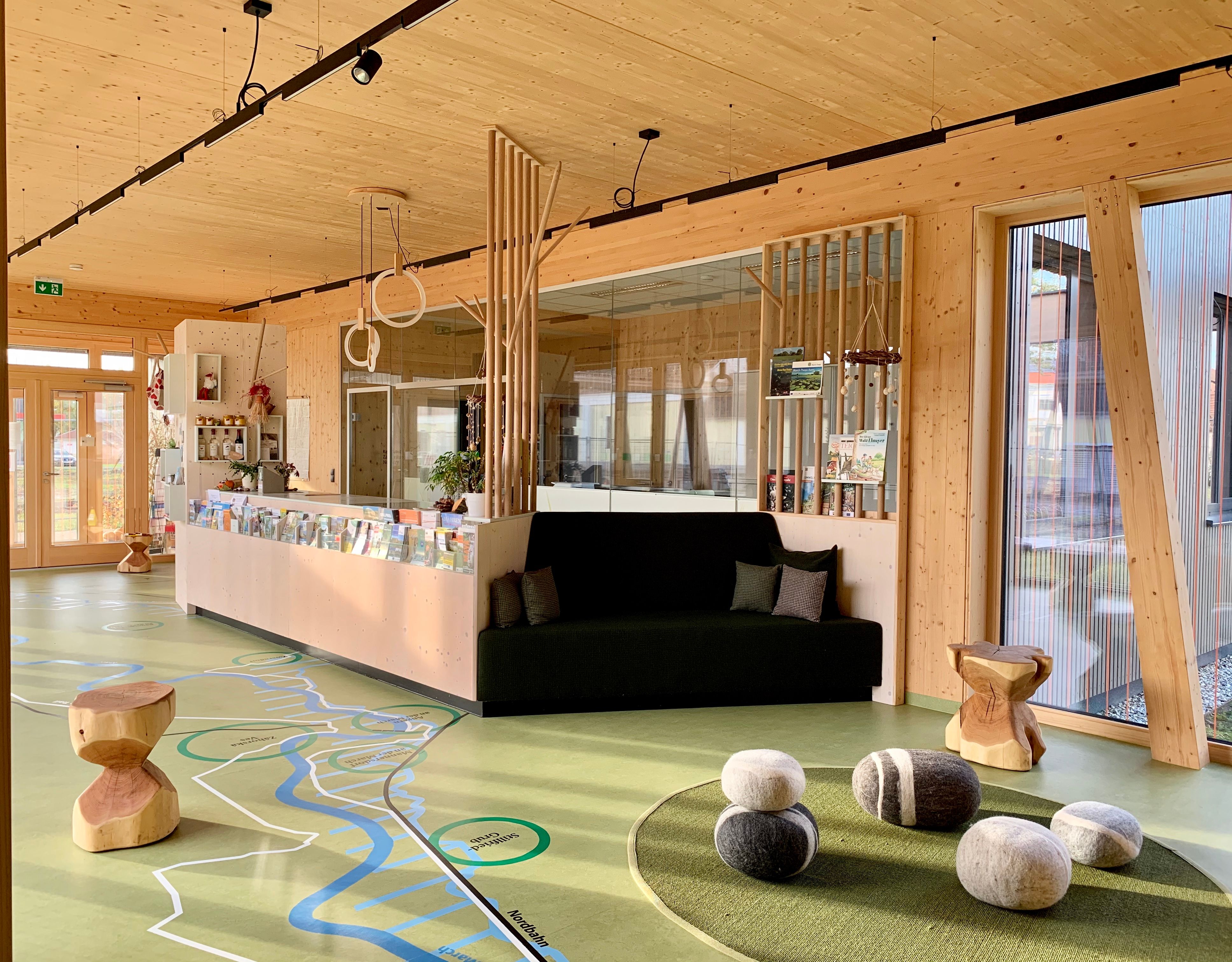 Innenansicht eines modernen Foyers mit Holzelementen, einer Sitzbank und dekorativen Steinen auf dem Boden.